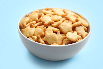 Delicious goldfish crackers in bowl on light blue background