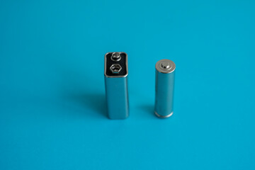 High voltage Volt 9V battery and alkaline AA battery on a blue background. Energy.