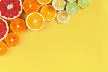 Slices of citruses are laid out in gradient composition in upper left corner of background. Tangerines, oranges, grapefruits, lemons, limes are lying on yellow canvas. Summer exotic tropical fruits.
