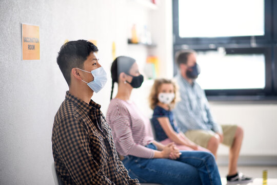 People With Face Masks In Waiting Room In Hospital, Coronavirus, Covid-19 And Vaccination Concept.