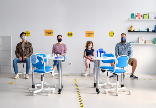 People with face masks in waiting room in hospital, coronavirus, covid-19 and vaccination concept.