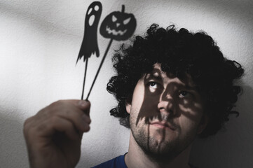 Portrait of an adult man in a black wig with shadows of Halloween pumpkin and a ghost on his eyes....