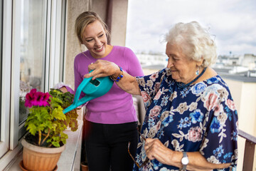 Senior woman and her adult granddaughter watering plants on the balcony

