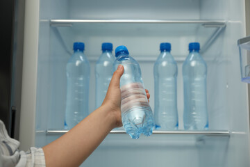 Woman with bottle of fresh water near open fridge, closeup