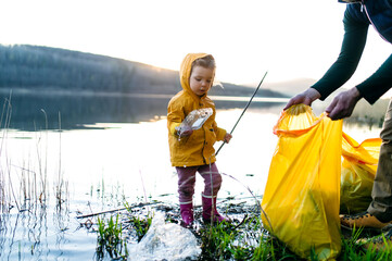 Father with small daughter collecting rubbish outdoors in nature, plogging concept.
