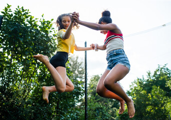 Low angle view of young teenager girls friends outdoors in garden, jumping on trampoline.