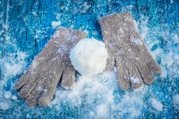 Snowball and mittens on a snowy wooden surface