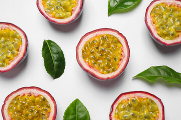 Halves of passion fruits (maracuyas) and green leaves on white background, flat lay