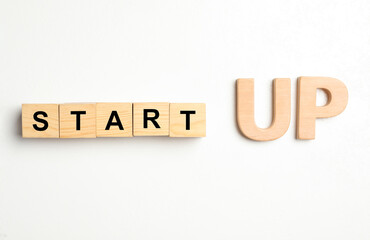 Words START UP made with wooden blocks on white background, flat lay