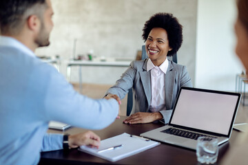 Happy black bank manager handshaking with her client during a meeting in the office.