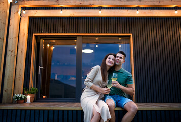 Young couple with wine outdoors, weekend away in container house in countryside.
