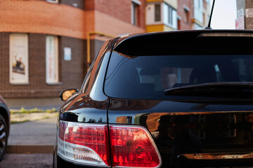 Back window of black car parked on the street in summer sunny day, rear view. Mock-up for sticker...