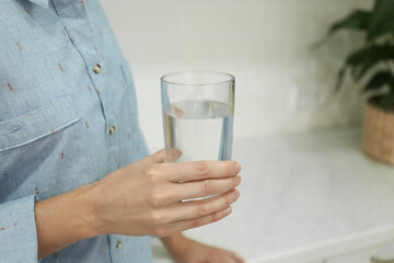 Woman holding glass of water at home, closeup
