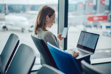 Young woman traveler using smartphone and laptop at airport
