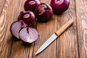 cut and whole red onion near knife on wooden table