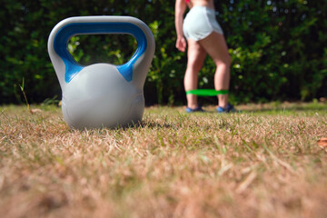 Fitness kettlebell woman cross training outside on crass lifting kettlebells and resistance band for squat - obrazy, fototapety, plakaty