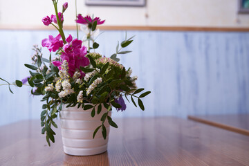 Colorful wildflowers stand in a White vase against a blue wall