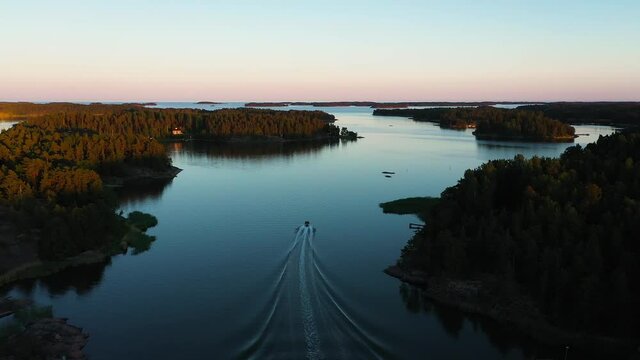 Aerial view following a boat, driving in middle of islands, colorful, summer sunset, in the Swedish Stockholm archipelago, at the Gulf of Bothnia, in Sweden - dolly, drone shot