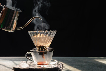 Steam from dripping coffee, Drip brewing is a method which involves pouring hot water over roasted filtered ground coffee beans in a filter  on old wood table and black background, Natural light.