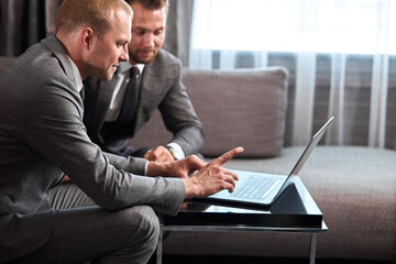 two confident business people work on laptop during business meeting, isolated in room,two young men in formal suit discussing