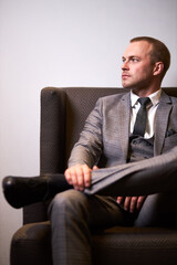 portrait of confident businessman sitting on chair, young caucasian male in formal elegant wear posing, looking away