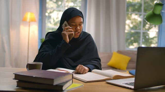 Female Muslim student enjoys studying reading book and talking on phone with classmate
