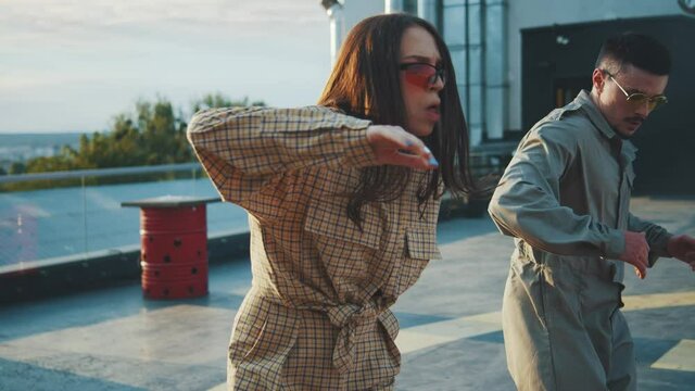 Two stylish hip-hop young people dancing on rooftop with sunset background. Male and female break dancers performing street underground dance together. Battle. Movement.