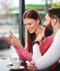Happy and loving couple in cafe with smartphone, having fun communicating