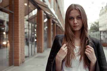 wide angle portrait blonde woman in casual black faux leather jacket. Female model wearing jacket over her sholders. Woman looking at the camera