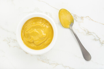 Mustard sauce in a bowl and spoon on white marble table. Top view