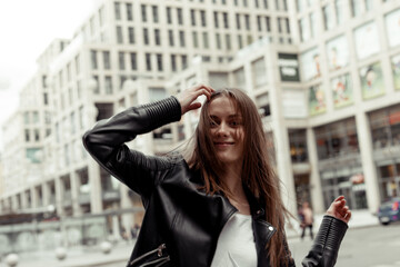 Blonde girl with long windy hair. Portrait of the girl in black faux leather jacket on the building...