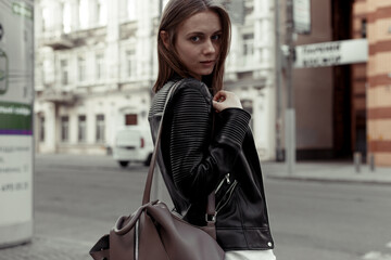 Woman with shoulder bag. Woman in a black leather jacket. Portrait on a blurred urban background. Outdoor.