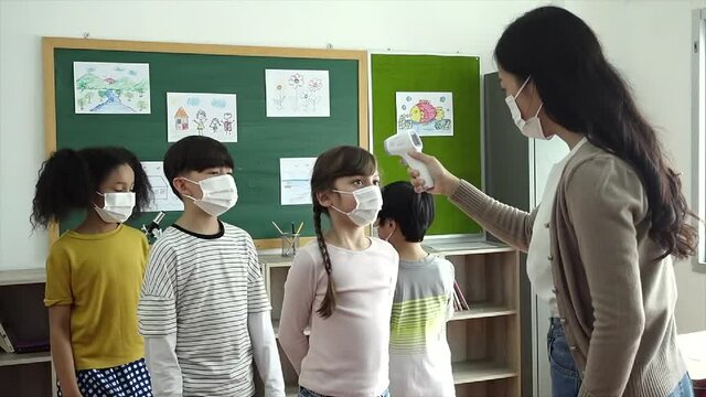 Group Of Elementary School Pupils With Face Mask Stood In Line Let The Teacher Check, Scan Thermometer Temperature For Fever Against The Spread Virus In Classroom After Covid-19 Quarantine, Lockdown.