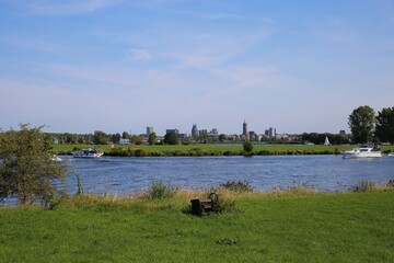 Roermond (city marina), Netherlands - August 9. 2020: View over green meadow and river on skyline of dutch city (focus on horizon)