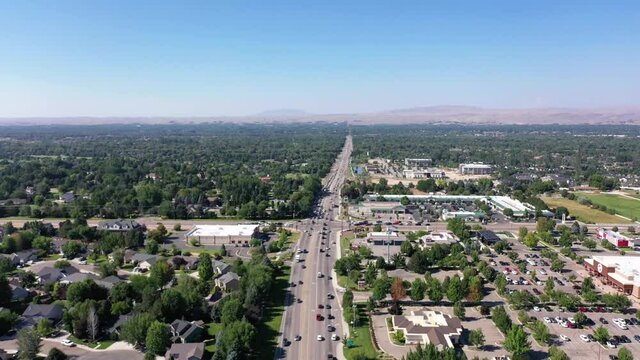 Drone pushes in and tilts down over a steady flow of traffic. There are lots of visible trees, homes and businesses.