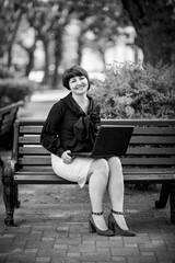 Obraz premium black and white portrait of a woman in business style, with a laptop, on a bench in the Park, working remotely in the field of Economics and accounting.