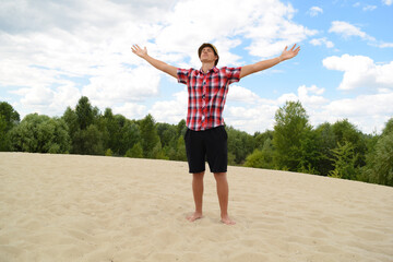 Obraz premium A young man in a bright checkered T-shirt stands with raised hands in nature