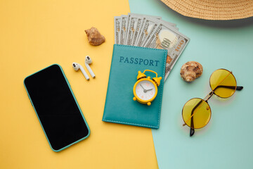 Summer vacation composition. Sunglasses, smartphone, hat and passport with money banknotes on blue yellow background.