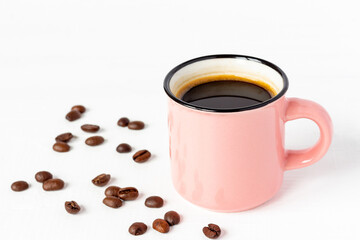 Pink сup of fresh coffee with grains on white wooden background.