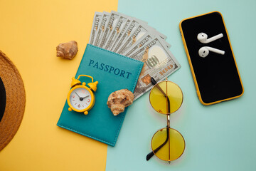 Summer vacation concept. Sunglasses, smartphone, hat and passport with money banknotes on blue yellow background.
