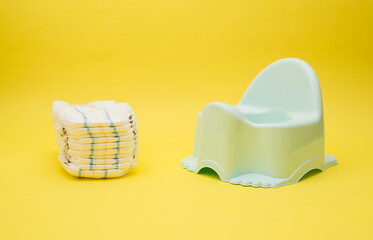 Baby diapers and potty on yellow background