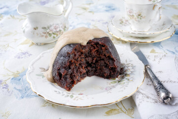 Traditional Australien plum pudding with vanilla rum sauce offered as close-up on a design plate