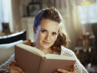 smiling woman in modern house in sunny winter day reading book