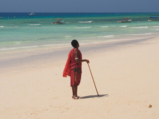Zanzibar island, Tanzania - 08/07/2020: African man is standing on the white sand beach, near blue Indian ocean
