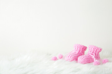Pink knitted fluffy baby socks on white fluffy fur blanket. Closeup. Empty place for text on light gray background. Front view.
