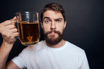 man with a mug of beer in a white t-shirt emotions lifestyle drunk on a dark isolated background
