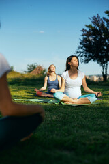 Two calm pregnant women sitting outdoors and meditating while their instructor showing them exercises.