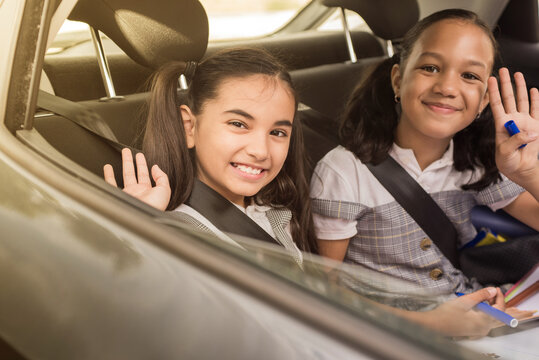 Little girls sitting on a backseat of a car looking camera going to school by car and waving goodbye. Transportation concept routine morning.