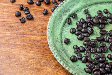 Top view of old green plate with coffee beans, on wooden table, horizontal, with copy space