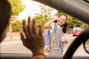 View from the car schoolgirl saying goodbye with the hand. Smiling latin girl waving goodbye to his mother before school.